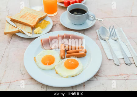 Frühstück mit gebratenes Ei, Schinken, Wurst, Toast, Marmelade, Butter, Wassermelone, Orangensaft und schwarzen Kaffee auf Marmortisch. Stockfoto