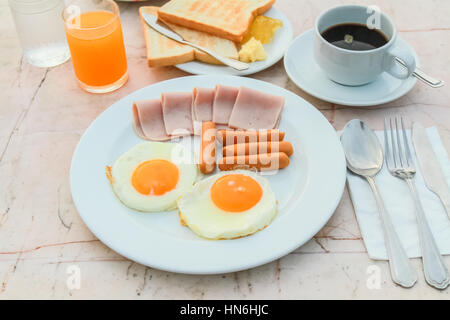 Frühstück mit gebratenes Ei, Schinken, Wurst, Toast, Marmelade, Butter, Wassermelone, Orangensaft und schwarzen Kaffee auf Marmortisch. Stockfoto
