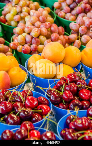 Frische Kirschen, Aprikosen und roten Trauben in Töpfen auf dem Display am Bauernmarkt Stockfoto