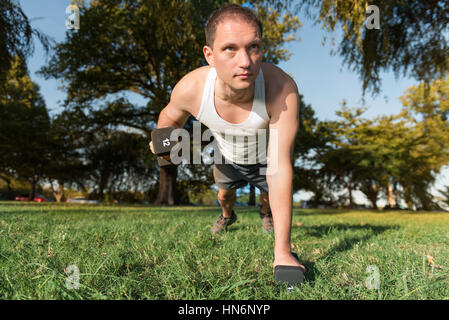 Junger Mann darstellende Hantel Reihe Übung 12 Pfund Gewicht in Grasgrün Outdoorpark heben Stockfoto