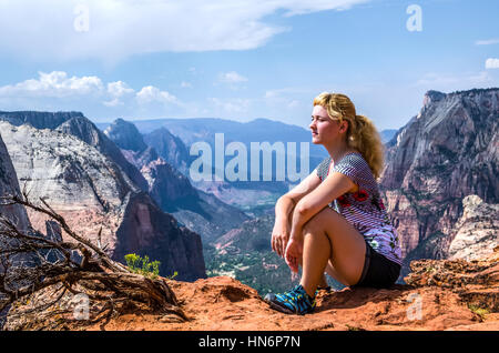 Junge Frau sitzt am Rand oben auf Canyon am Observation Point Trail in Zion Nationalpark Stockfoto