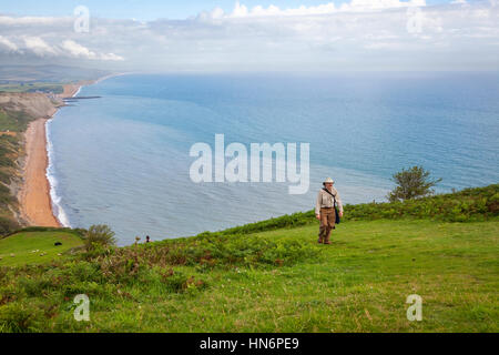 Ein Mann Klettern eines langen Hügels mit dem Atlantischen Ozean im Hintergrund entlang der South West Coast Path in Dorset, England. Stockfoto