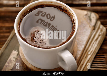 Tasse Kaffee und alte Buch auf hölzernen Hintergrund mit guten Morgen Inschrift Stockfoto