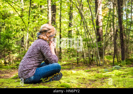 Junge Frau sitzt auf moosigen Boden im Wald denken Stockfoto