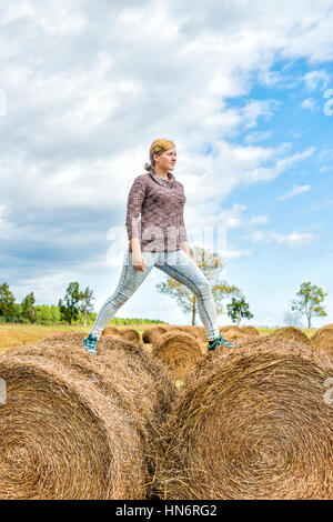 Junge Frau balancieren auf Heuballen roll Stockfoto