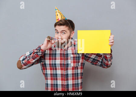 Foto von fröhlichen jungen bärtigen Geburtstagskind Exemplar Board stehend über grauen Hintergrund zu halten. Stockfoto