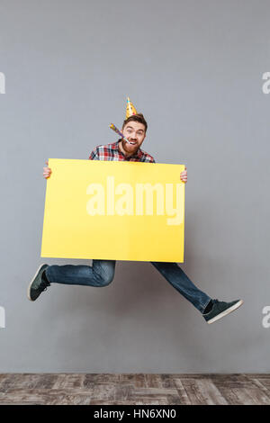 Bild von Geburtstag junge bärtige Mann, hält Exemplar Board springen über grau hinterlegt. Stockfoto