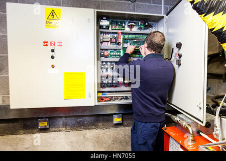 Ein Elektriker, der an einer elektronischen Bedienkonsole in einem Schaltkasten arbeitet Stockfoto