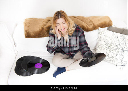 Junge blonde Frau glücklich genießen Musik hören von Vintage Vinyl-Schallplatten auf Sofa im Wohnzimmer Stockfoto