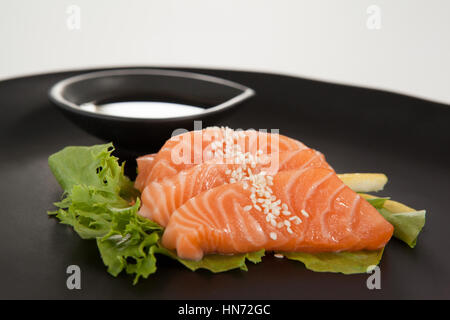 Nahaufnahme von vier Sashimi Sushi mit Sojasauce in schwarze Platte serviert Stockfoto