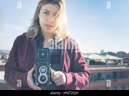 Junge schöne, faszinierende Frau mit alten Vintage Rolleflex-Kamera und Rom Skyline im Hintergrund Stockfoto