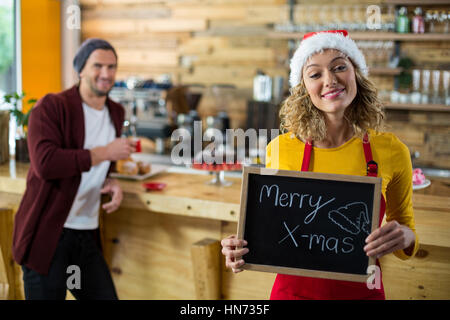 Porträt von lächelnden Kellnerin stehend mit merry X-Mas-Schild im café Stockfoto