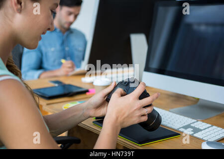 Weibliche Grafiker überprüfen aufgenommenen Bilder in seiner Digitalkamera am Schreibtisch im Büro Stockfoto