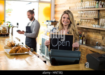 Lächelnde Kellnerin stehen am Tresen und zeigen Schiefer mit Schild "geöffnet" in CafÃƒÂ © Stockfoto