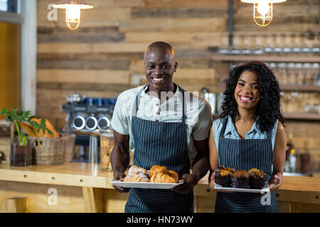 Porträt von Kellner und Kellnerin, die Halteplatte der Cupcake und Croissant am Schalter im CafÃƒÂ © Stockfoto