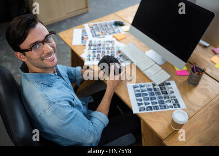 Porträt des Menschen sitzen am Schreibtisch hält Digitalkamera im Büro Stockfoto