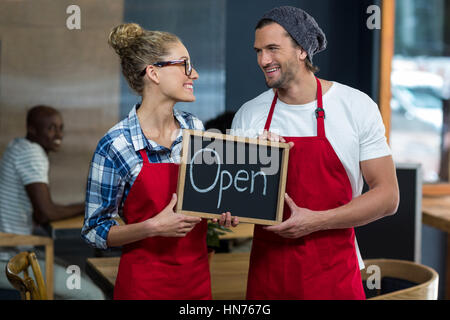 Lächelnde Kellnerin und Kellner stehend mit Schild "geöffnet" Board in CafÃƒÂ © Stockfoto