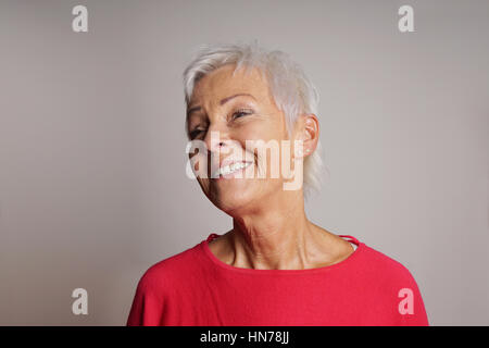 glückliche ältere Frau mit trendigen kurze weiße Haare zu lachen. Grauer Hintergrund mit Textfreiraum. Stockfoto