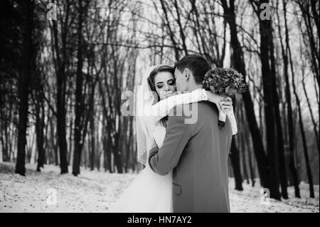 Junge stilvolle Hochzeitspaar im Wald am Wintertag. Liebe Brautpaare auf Schneewetter. Schwarz / weiß Foto. Stockfoto