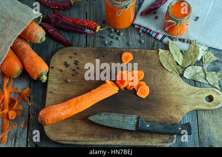 Geschnitten Sie in Runde Scheiben eine große frische Karotten auf ein Schneidebrett mitten in Gemüse und Gewürzen Stockfoto