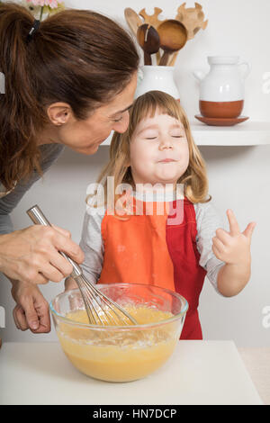 drei Jahre alt Schlagsahne Kind saugen ihre Finger nach Geschmack, neben Frau, in Teamarbeit, machen und kochen ein Rührkuchen in Küche nach Hause Stockfoto