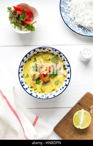 Thai Kokosmilch Suppe mit Hühnerfleisch, Pilzen, Koriander, Paprika und Reis Nudeln in bunte Schüssel auf weißen Tisch. Ansicht von oben. Stockfoto