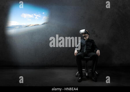 Geschäftsmann ruht auf Stuhl in einigen Hangar mit Virtual-Reality-Kopfhörer mit schönen Landschaft Projektion Stockfoto