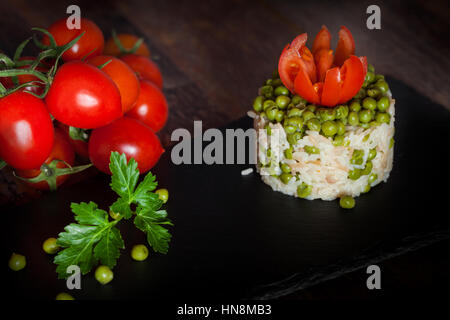 Portion Risotto mit Erbsen auf Schiefer Teller, dekoriert mit Tomaten und Petersilie. Stockfoto