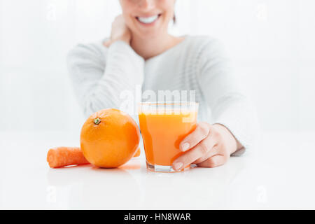 Lächelnde Frau trinkt eine gesunde natürliche Saft gemacht mit Orangen und Karotten, gesunde Ernährung und Vitamine-Konzept Stockfoto