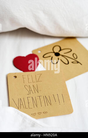 Nahaufnahme von einem braunen Papier-Schuldbrief mit Text Feliz San Valentin, happy Valentinstag geschrieben in Spanisch und eine Blume in einer anderen Anmerkung und ein rot gezeichnet Stockfoto