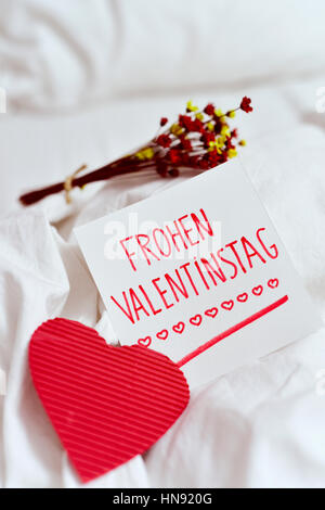 Nahaufnahme von einem roten Herzen, ein weiß Papier-Schuldbrief mit Text Frohen Valentinstag, happy Valentinstag in Deutsch und eine Reihe von Trockenblumen auf th geschrieben Stockfoto