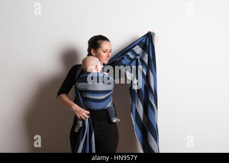 Schöne junge Mutter Umhüllung ihres Sohnes in Sling. Studio gedreht. Stockfoto