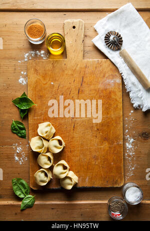 Hausgemachte rohe italienische Tortellini und Basilikum Blätter auf dunkle Vintage-Hintergrund Stockfoto