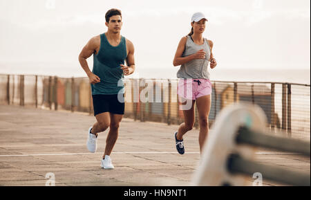 Zwei Läufer laufen entlang der Straße am Meer. Fitnesspaare joggen auf der Strandpromenade. Stockfoto