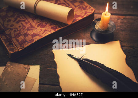 Vintage Feder mit Papier und alten Buch auf Tisch im Licht der Kerze Stockfoto