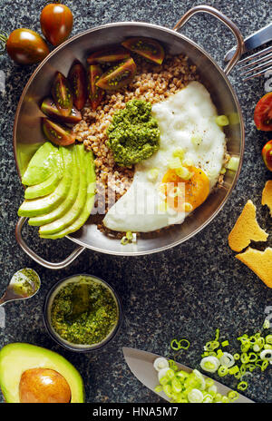 Frühstück mit Eiern, Avocado, Salat mit Tomaten, Pesto und Buchweizen in einer Pfanne auf dem Tisch Stockfoto