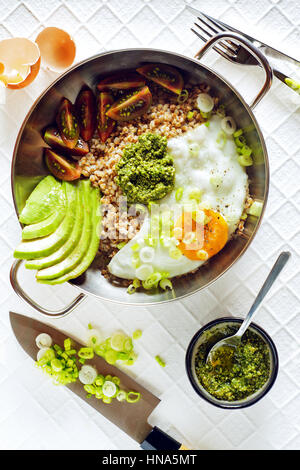 Frühstück mit Eiern, Avocado, Salat mit Tomaten, Pesto und Buchweizen in einer Pfanne auf dem Tisch Stockfoto