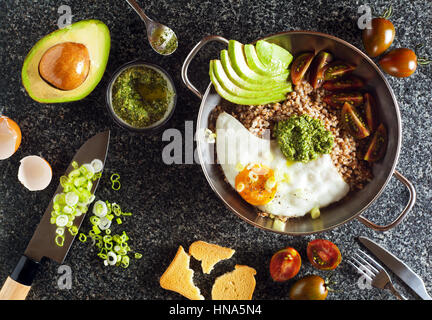 Frühstück mit Eiern, Avocado, Salat mit Tomaten, Pesto und Buchweizen in einer Pfanne auf dem Tisch Stockfoto