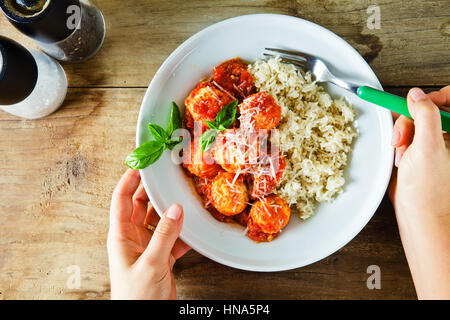 Frikadellen aus Ricotta-Käse und gekochten Reis mit Tomatensauce auf Holztisch. die Hände von Frauen Stockfoto