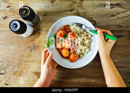 Frikadellen aus Ricotta-Käse und gekochten Reis mit Tomatensauce auf Holztisch. die Hände von Frauen Stockfoto