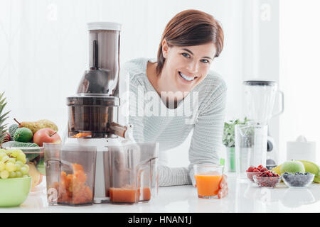 Lächelnde junge Frau trinken gesunde Saft mit frischem Obst und Gemüse gemacht, nutzt sie einen Entsafter Stockfoto