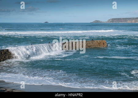 Starke Winde fahren Wellen über der Oberseite von der Mole in Sennen Cove, Cornwall, England. Großbritannien Wetter. Stockfoto