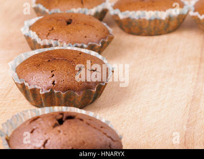 Schoko-Muffin. Reihe von frisch gebackenen Schokoladen-Muffins in Papier Backen Form auf Holzbrett Stockfoto