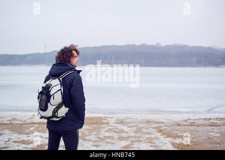 Reist der lockige Haare Mann in eine Jacke mit Rucksack Winter am See Stockfoto