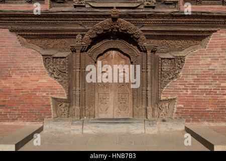 Eine reich geschnitzte Holztüre, geschmückt mit Figuren von Hindu-Götter und himmlische Kreaturen auf einem Backsteingebäude in Bhaktapur, Kathmandu Stockfoto