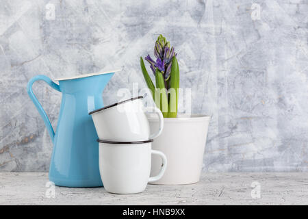 Zwei weiße Emaille Becher, blaue Kanne und blühenden Blume Hyazinthe im Topf auf hellem Hintergrund Stockfoto