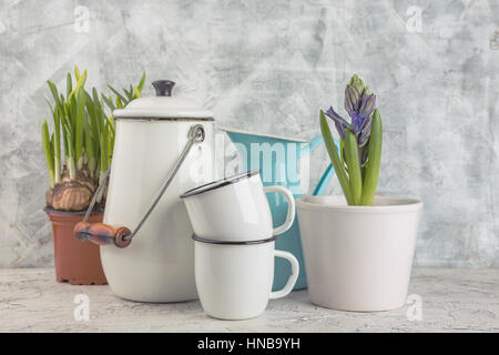 Zwei weiße Emaille Becher, blaues Glas, weiße Dose und Frühling Blumen im Topf auf hellem Hintergrund Stockfoto