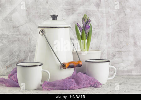 Zwei weiße Emaille Becher weiße Dose und blühende Blume Hyazinthe im Topf auf hellem Hintergrund Stockfoto