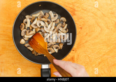 Man rührt Champignons in Pfanne auf Schneidebrett Stockfoto
