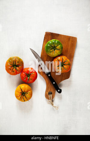 bunte Tomaten auf Schneidebrett auf weißem Hintergrund und Messer Stockfoto